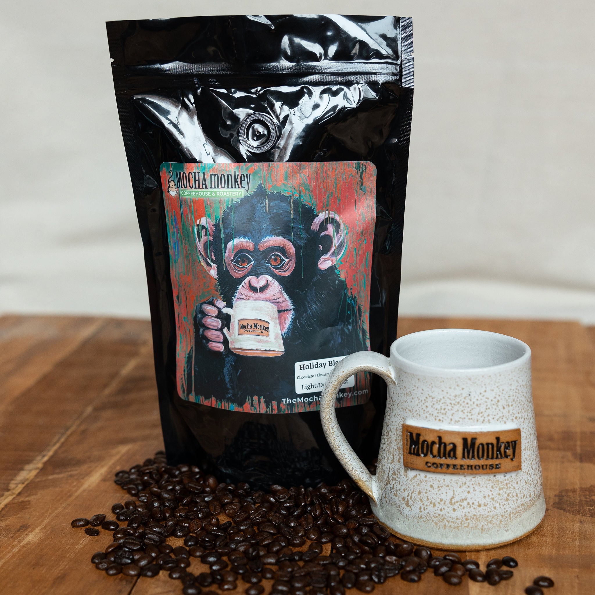 Bag of Mocha Monkey Holiday Blend roasted coffee seen with a Moch Monkey branded hand-made mug