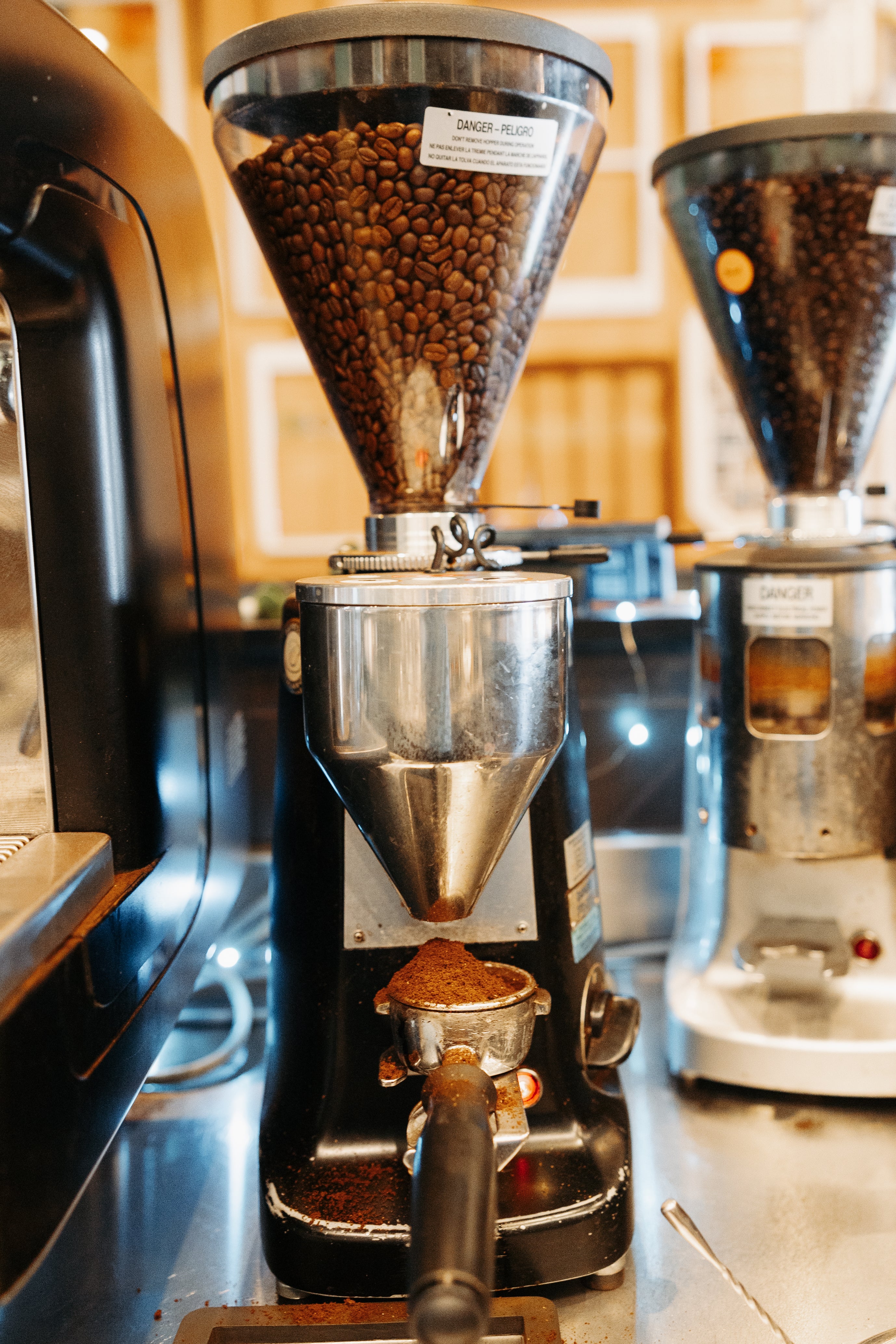 Coffee grinder filled with espresso beans and an espresso machine portafilter filled with ground coffee 