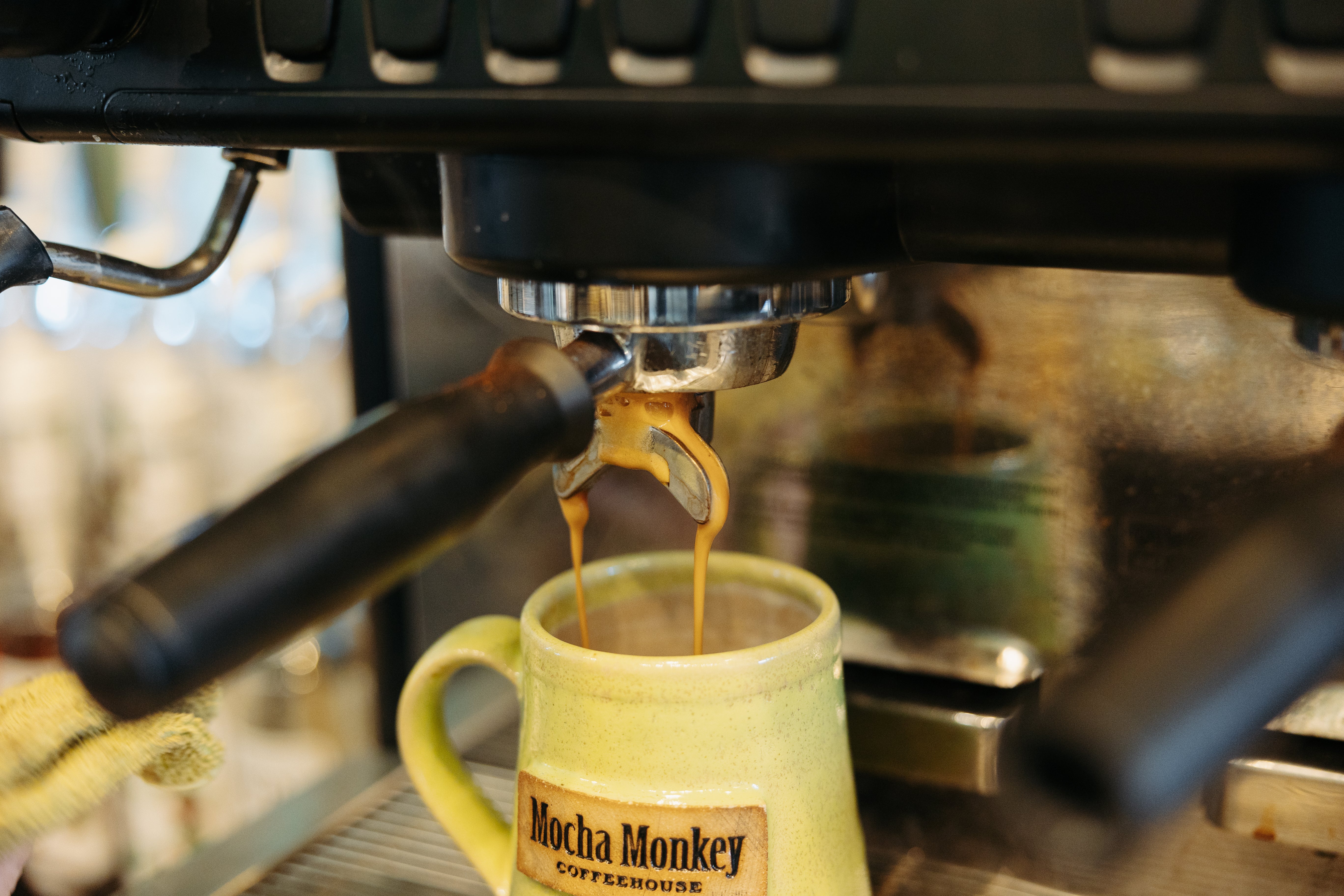 Espresso machine filling a handmade yellow pottery Mocha Monkey Coffeehouse branded mug