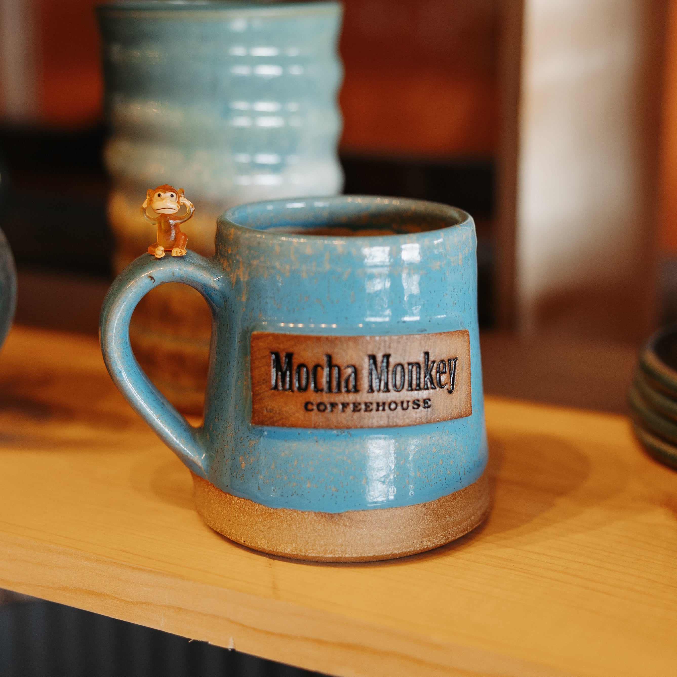 Blue handmade pottery mug with a tiny monkey on the handle branded with Mocha Monkey Coffeehouse