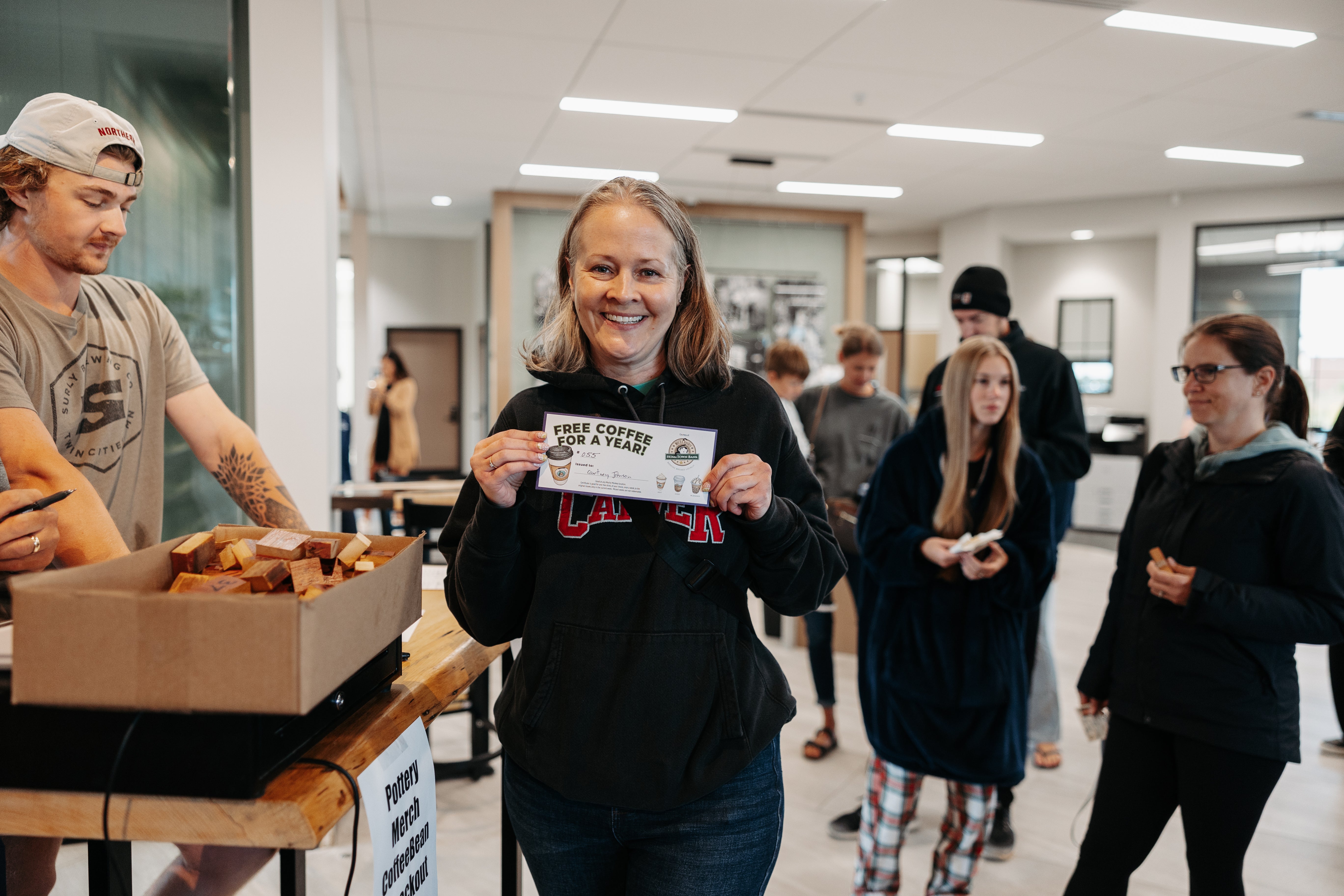 Woman holding up her "Free Coffee for a Year" gift certificate which she received at the Grand Opening of the Mocha Monkey Coffeehouse in Carver