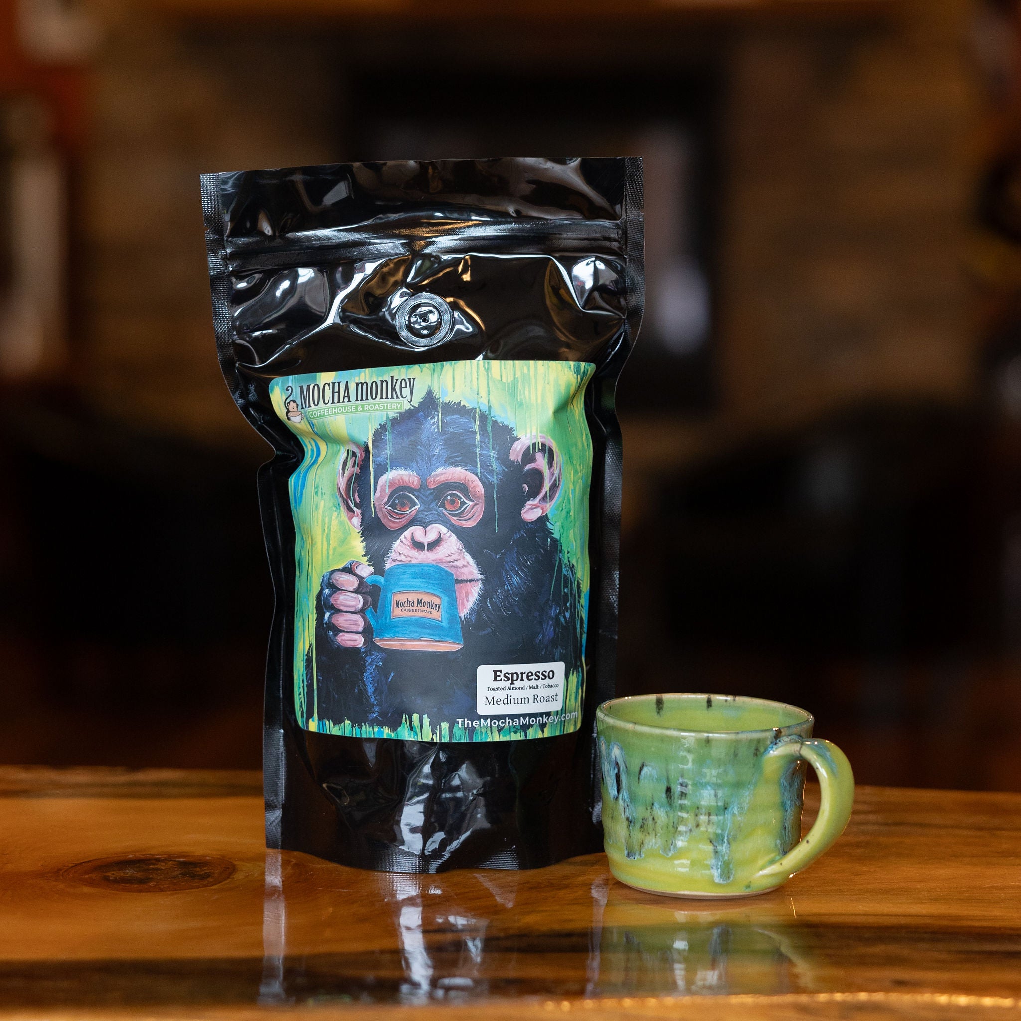 A 12oz bag of Mocha Monkey Espresso on a table with a green mug