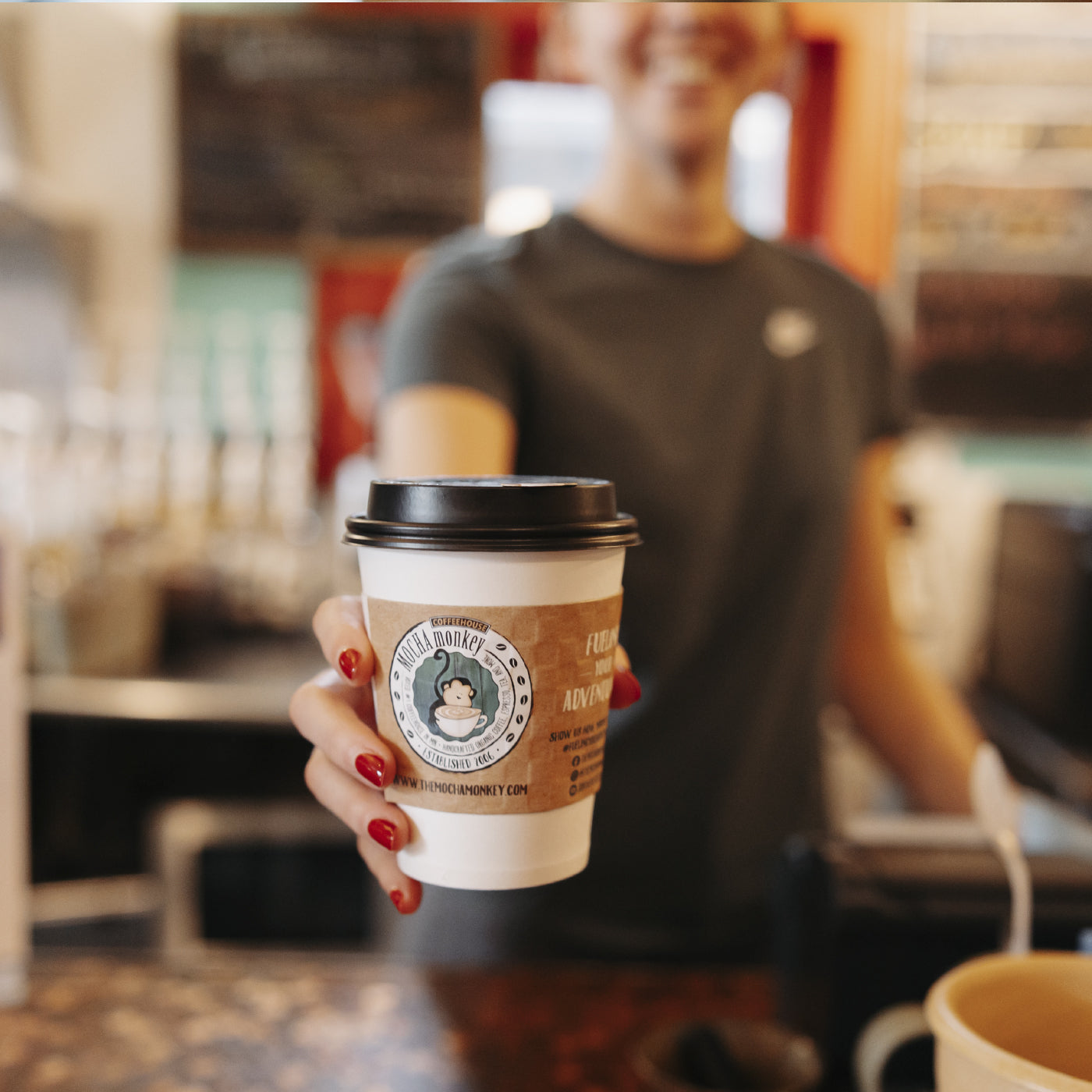 A Barista holding out a cup with a Mocha Monkey branded slee