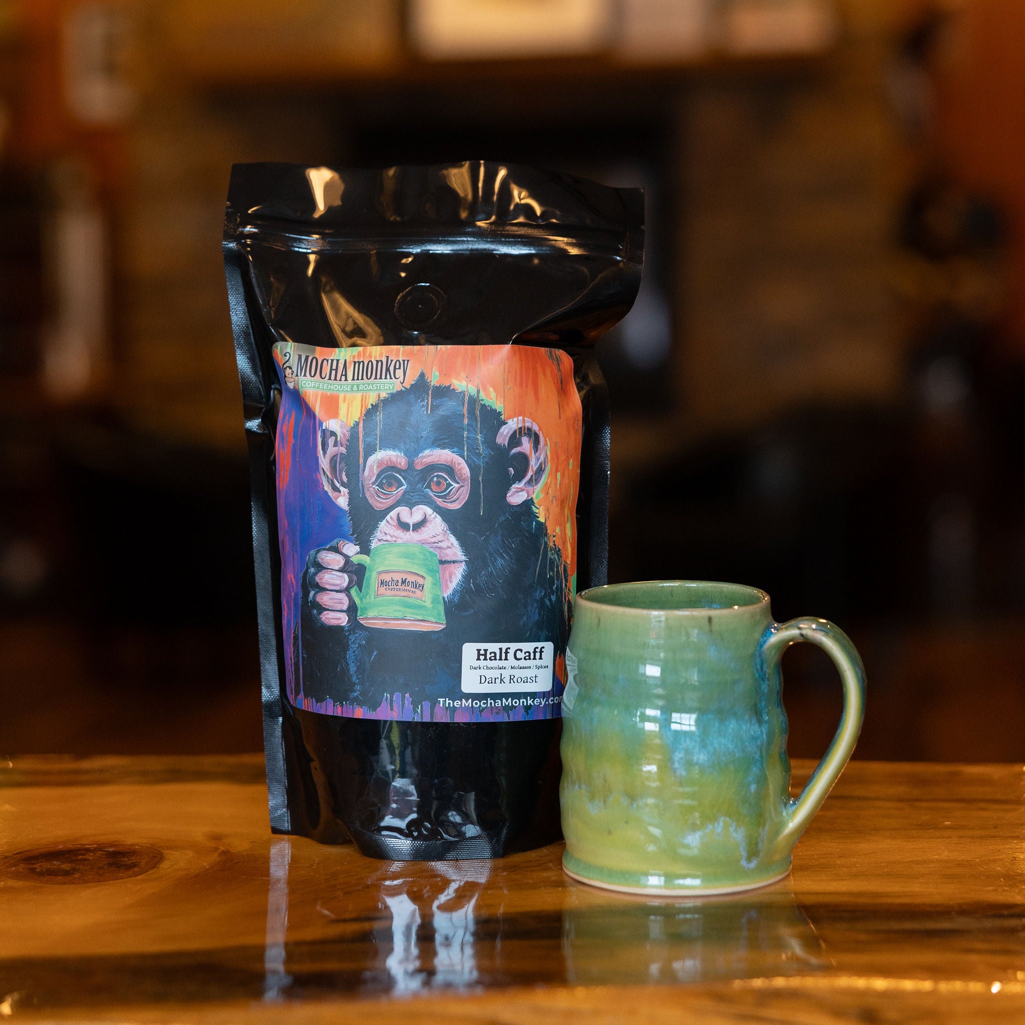 A 12oz bag of Mocha Monkey Half Caff on a table with a mug