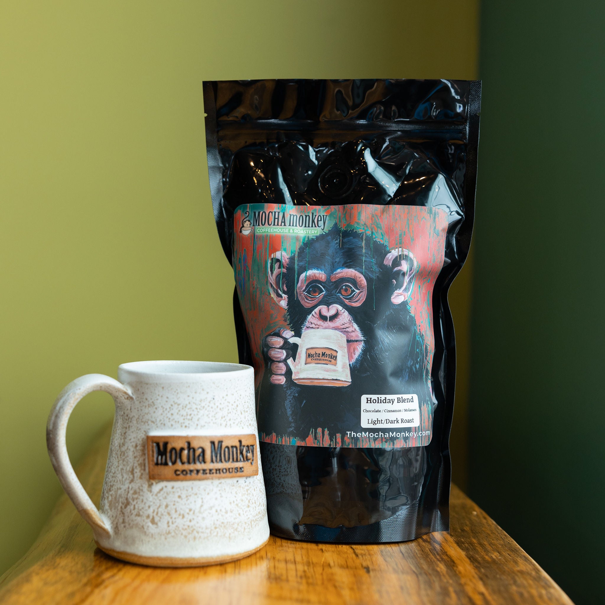 A 12oz bag of Mocha Monkey Holiday Blend on a shelf with a Mocha Monkey Coffeehouse branded mug