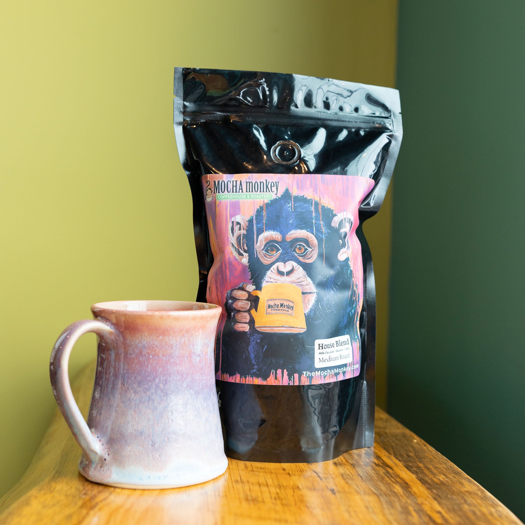 A 12oz bag of Mocha Monkey House Blend on a shelf with a mug