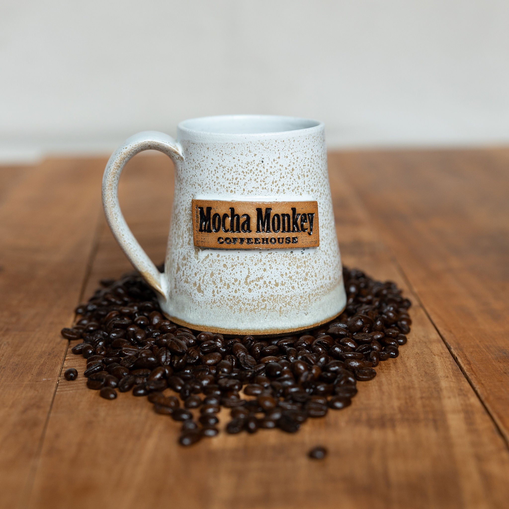 A Mocha Monkey branded handmade pottery mug on a table surrounded by coffee beans